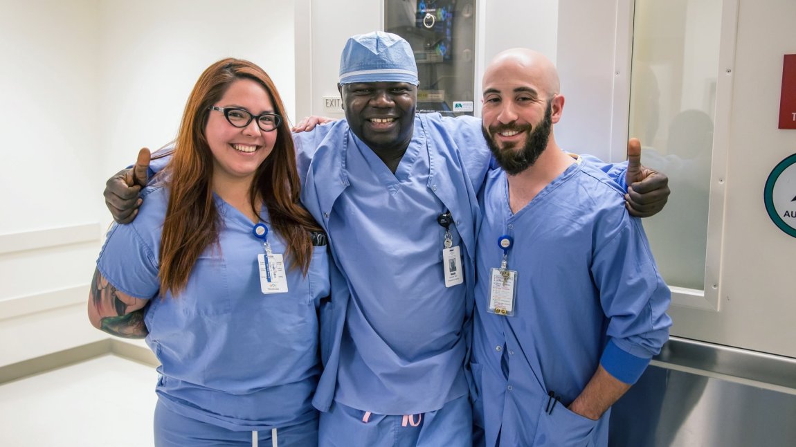 Group of three nurses in blue scrubs giving thumbs up